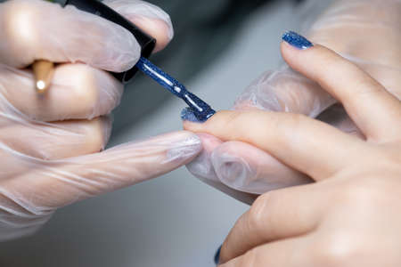 the manicure master applies the final layer of gel polish to the client's nail
