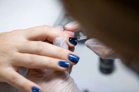 close-up, the master evens the color of the manicure with blue, applying gel polish on it with a brushの写真素材