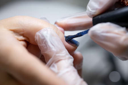 close-up of a nail on which a blue gel polish is applied distributing it with a manicure brush over the surfaceの写真素材