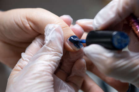 close-up of a nail on which a blue gel polish is applied distributing it with a manicure brush over the surfaceの写真素材