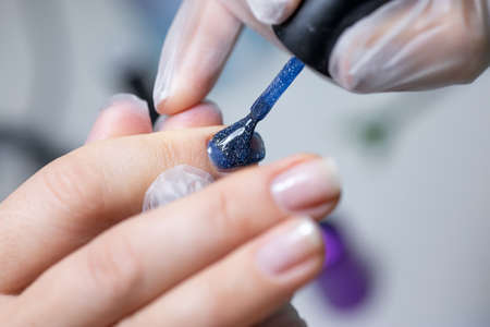 close-up of a nail on which a blue gel polish is applied distributing it with a manicure brush over the surfaceの写真素材