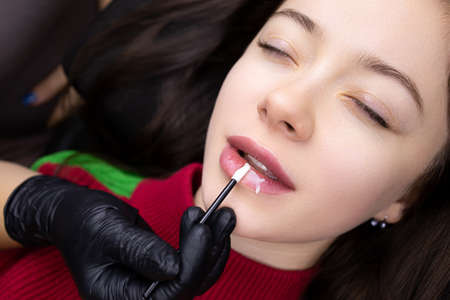 the model girl is lying on the couch and the master applies oil to her lips after permanent makeupの写真素材