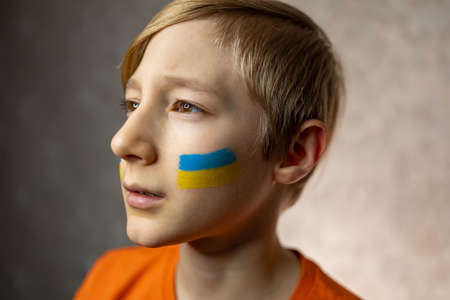 a child against war, a portrait of a boy with a painted flag of Ukraine on his cheeks proudly looks awayの写真素材