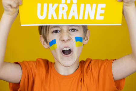 a boy with a painted flag of Ukraine on his cheeks pulled out a poster with the inscription Ukraine over his headの写真素材