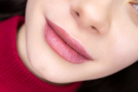 the completed procedure of permanent lip makeup girl model is lying on the couch