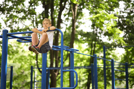 a boy in the park goes in for sports climbed onto the pull-up bar and tucked his legs
