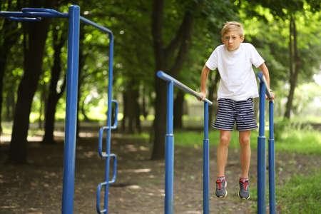 athlete boy in the park on the crossbar for push-ups grimaced and tries to perform the exercises