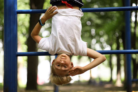 the boy athlete on the sports ground in the park caught his feet on the stairs and hangs upside down...