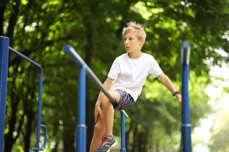 sports boy hung on the crossbar holding his hands and tucked his legs in front of himの写真素材
