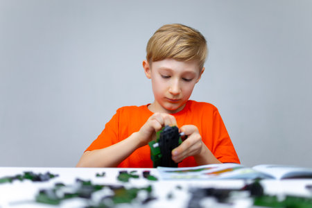 a boy plays with a plastic constructor examines the instructions for assembling a model