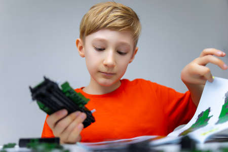 a boy plays with a plastic constructor examines the instructions for assembling a model
