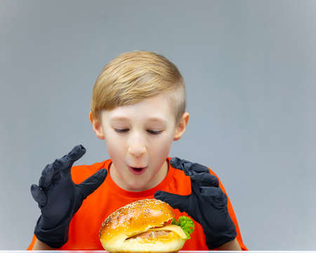 a boy with a cheeseburger looks at him and wants to take it in his handsの写真素材