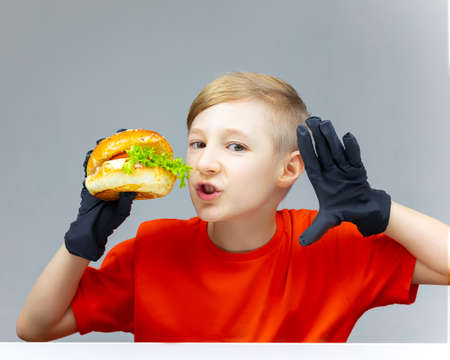 The boy is holding a burger in front of him. He has black gloves on his hands.の写真素材