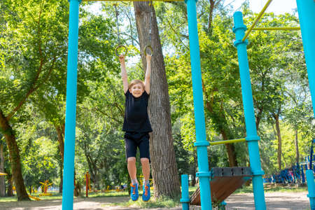 the boy goes in for sports in the park he hangs on the gymnastic rings and tries to pull himself up