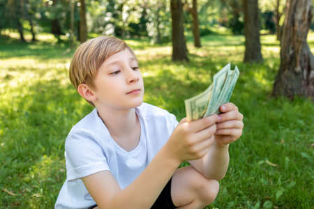 a boy in a white t-shirt holds dollar bills in front of him and looks at themの写真素材