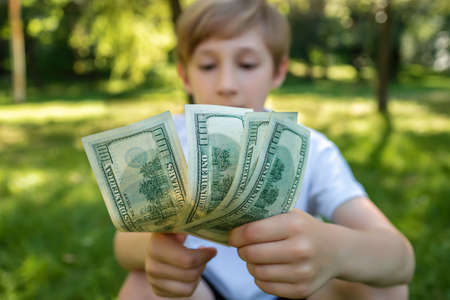 dollar bills in the foreground hold a boy against a blurred background in the parkの写真素材