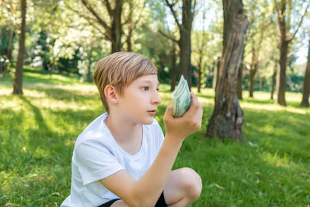 pensive boy squatting in the park holding dollar billsの写真素材