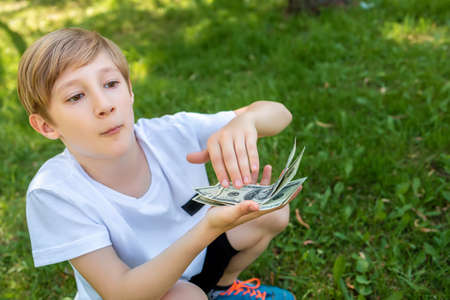 a boy squatting holding dollar bills in front of him brushes them forward from a pileの写真素材