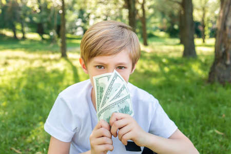 a boy in the park covered his face with dollar bills and looks menacingly aheadの写真素材