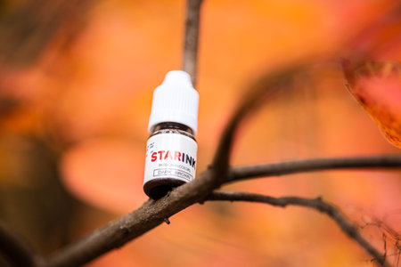 beautiful autumn blurred background with red leaves on the branches of which stands a bottle with...