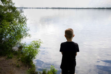 the boy stands with his back and looks at the river