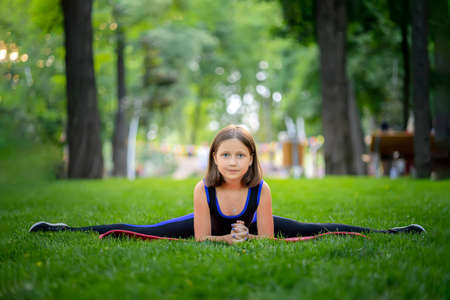 in the park, a little girl performs a frog element, doing stretching on a matの写真素材