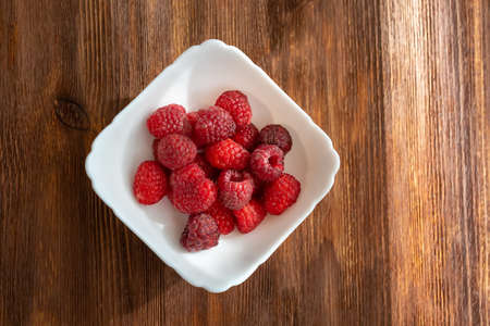 there is a white plate with raspberries on a wooden table