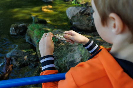 a boy in nature near the river is removed the hook of a caught fishの写真素材