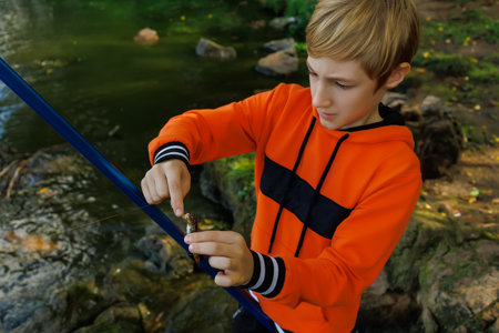 a boy in nature near the river is removed the hook of a caught fishの写真素材