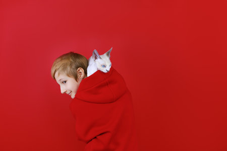 boy dressed in a red tracksuit with a cat on his shoulders on a red backgroundの写真素材