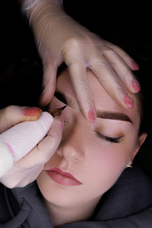 Beautiful girl model on the procedure of permanent makeup of the eyebrows, top view.