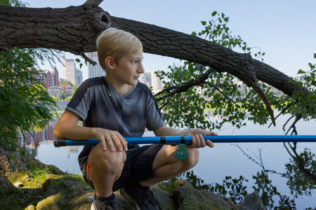 A boy squats on rocks and catches fish. Sport fishing on the river in summer.の写真素材