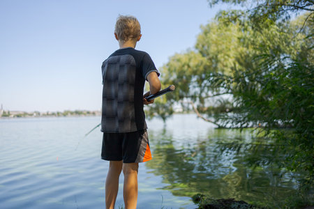 A teenager with his back turned is fishing with a cast rod. Sport fishing on the river in summer.の写真素材