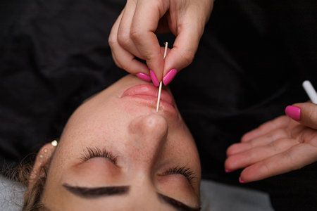 The master makes the Marking on the lips with a cotton swab. Delicate permanent lip makeup for blondesの写真素材