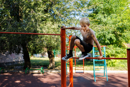 Athletic teenager wants to jump off the top of the bar. Street workout on a horizontal bar in the school park.の写真素材