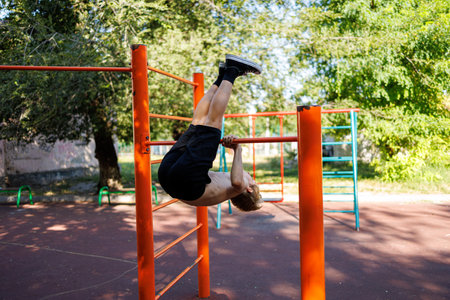 Athletic boy performs exercises on the bar. Street workout on a horizontal bar in the school park.