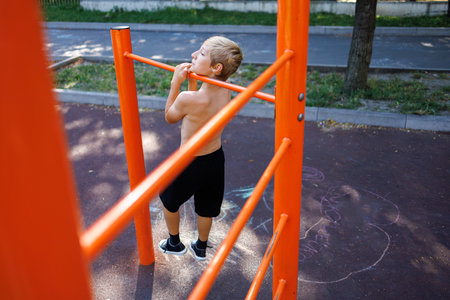 A teenager pulls himself up on the bar between the sports bars Street workout on a horizontal bar in the school park.の写真素材