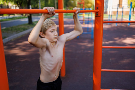 A teenager with athletic muscle development holds on to a bar. Street workout on a horizontal bar in...