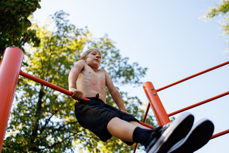 Bottom view of a teenage gymnast who performs the elements. Street workout on a horizontal bar in the school park.の写真素材