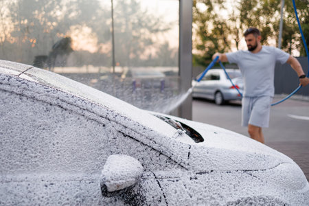 The hood and windshield of the car are covered with foam, the man in the background is applying foam to the car. A car at a self service car wash.の写真素材