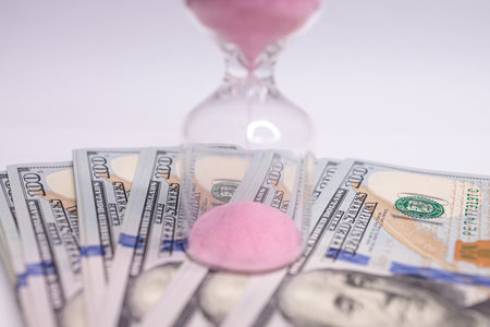 On the hourglass the time flows on the bills. The hourglass is located near the dollar bills.