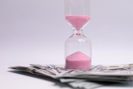 The hourglass is located near the dollar bills.の写真素材