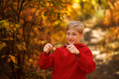In the fall in the park, a boy tries to break a twig. A boy in a red suit in a park in the fall.