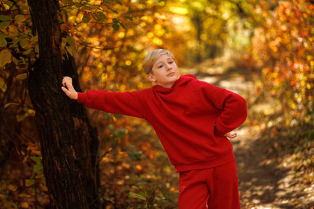 In a beautiful park, a child leaned his hand on a tree. A boy in a red suit in a park in the fall.の写真素材