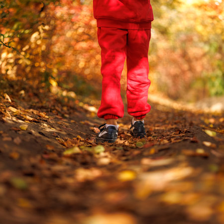 Back view of the legs of a boy walking through a park. A boy in a red suit in a park in the fall.の写真素材