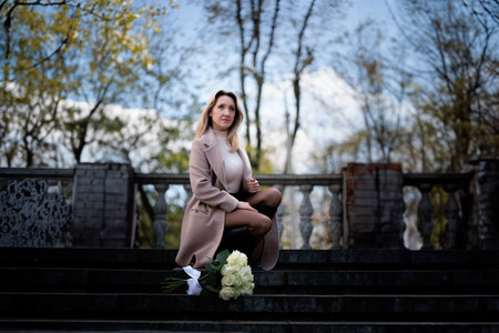 passive business woman near the stone stairs. Stylish woman in a coat in autumn with a bouquet of...