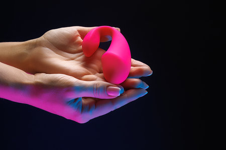 In the girl's hands is a red intimacy toy. Sex toy clitoral vibrator on a black background with neon lights.の写真素材