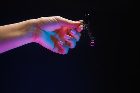 Close-up of a girl's hand holding a clothespin for juicing and intimate play with her fingers. Sex toy nipple clamp on black background with neon lights.の写真素材