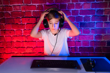 A teenager is playing. A gamer boy plays computer games against a neon lit brick wall.の写真素材