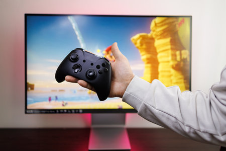 In the background of a video game monitor, a man's hand holds a controller in the palm of his hand....